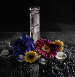 A sleek perfume bottle surrounded by vibrant flowers and water droplets in a studio setting.