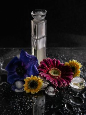 A sleek perfume bottle surrounded by vibrant flowers and water droplets in a studio setting.