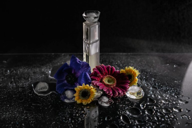 A sleek perfume bottle surrounded by vibrant flowers and water droplets in a studio setting.