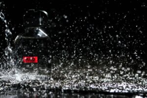 Close-up of water droplets splashing on a glass perfume bottle against a black background.