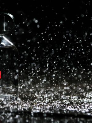 Close-up of water droplets splashing on a glass perfume bottle against a black background.