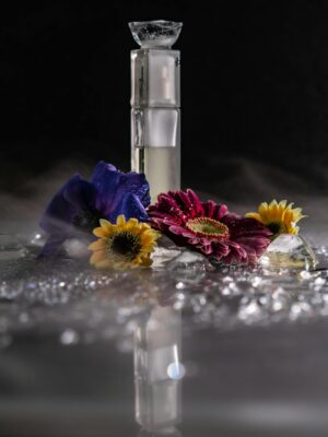 Dramatic still life of a perfume bottle surrounded by vibrant flowers and reflections, creating a mysterious ambiance.