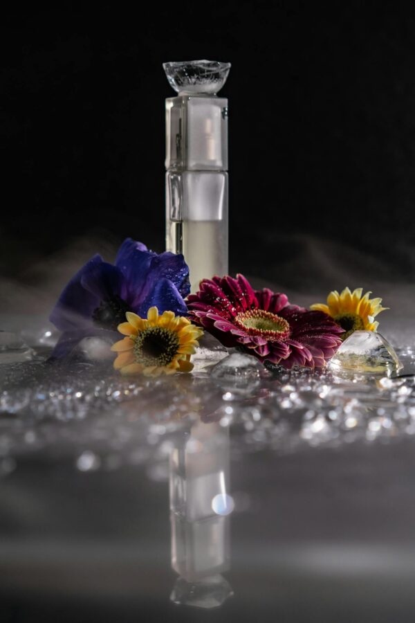 Dramatic still life of a perfume bottle surrounded by vibrant flowers and reflections, creating a mysterious ambiance.